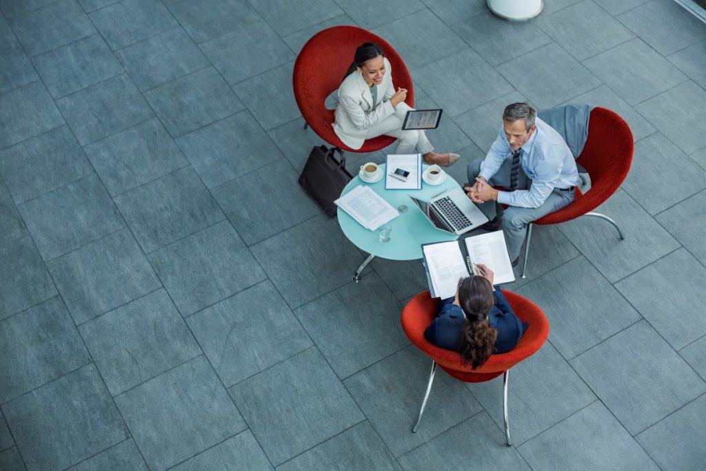 Three executives sitting on red chairs around a circular glass table.